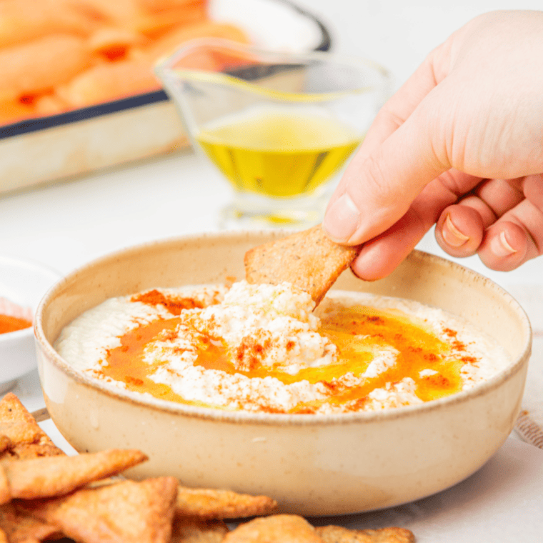 A bowl of creamy keto hummus garnished with olive oil, paprika, and parsley, served with fresh vegetables for dipping.