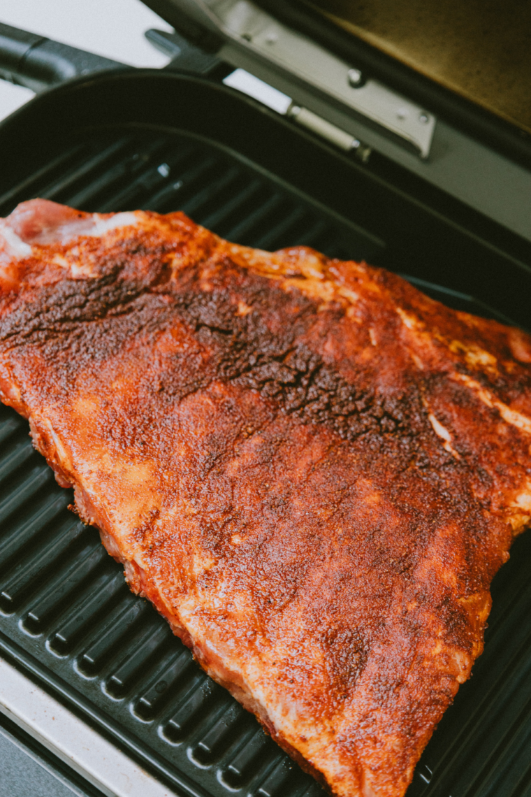 Carefully unwrapping grilled ribs and brushing both sides with BBQ sauce before finishing on high heat until caramelized and lightly charred