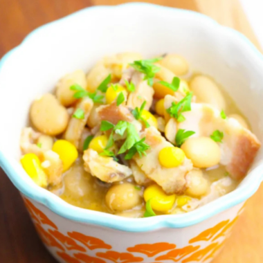 White ceramic bowl of slow cooker turkey white bean chili topped with shredded Monterey Jack, sour cream, and fresh cilantro