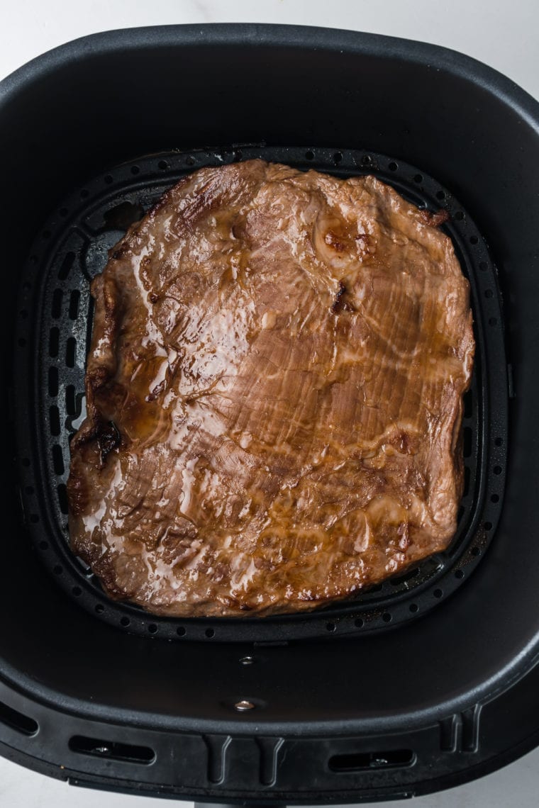 Preheating air fryer to 400°F, cooking marinated steak for 8-10 minutes, then resting and slicing against the grain.