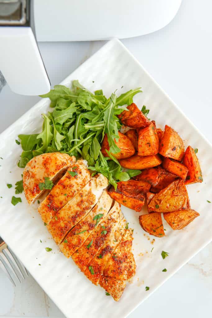 overhead: sliced chicken breast on plate with sweet potatoes and arugula salad
