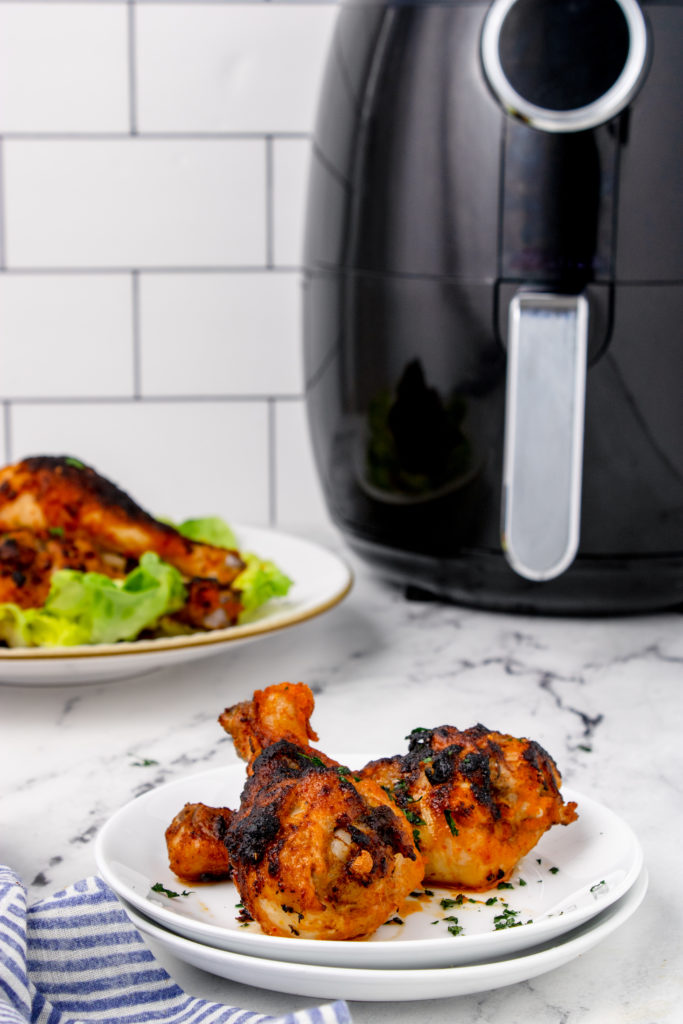 Finished product of chicken drumsticks in the air fryer with an air fryer in the background 