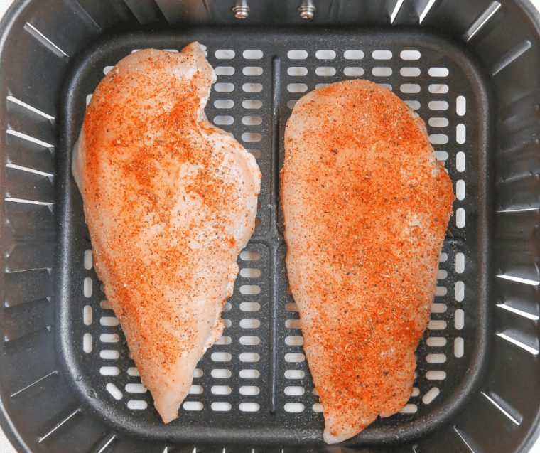two seasoned chicken breast in air fryer basket