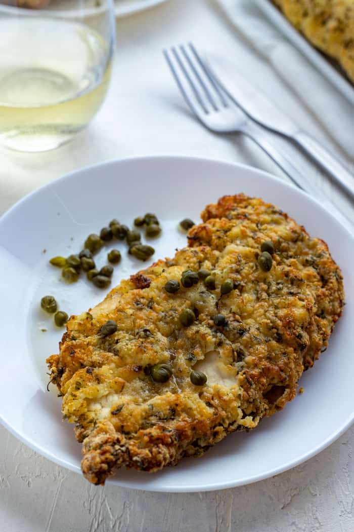 close up: crispy chicken cutlet on plate with capers