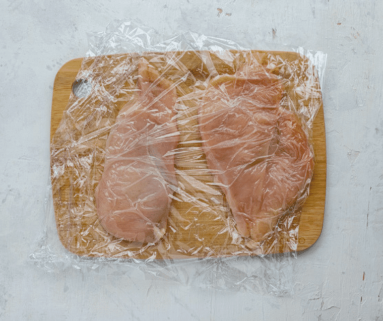 chicken cutlets wrapped in plastic wrap on cutting board