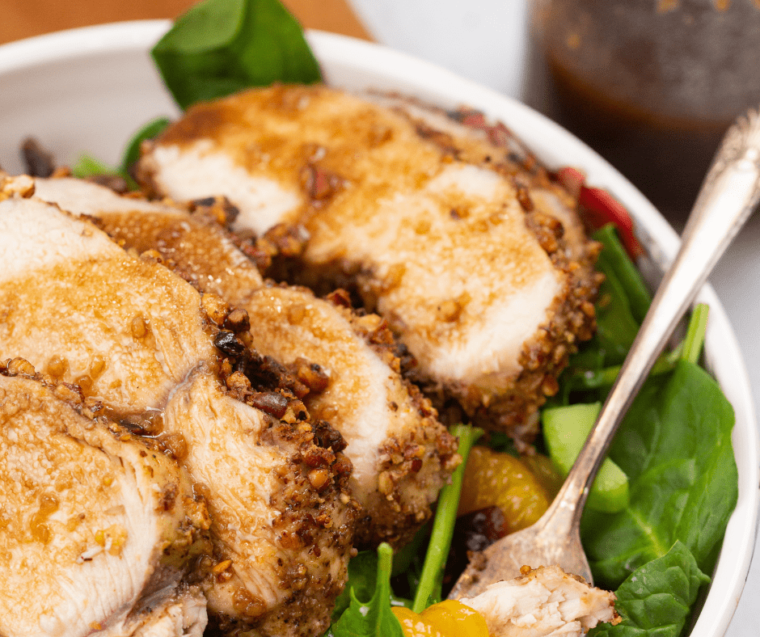 close up: sliced chicken coated in pecans on bed of spinach with mandarin oranges
