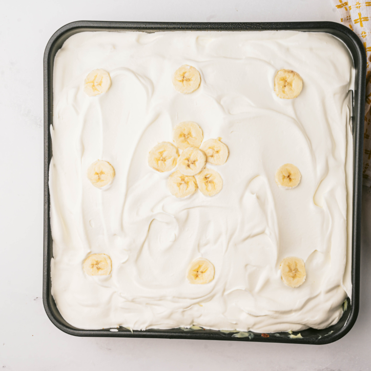 "Freshly baked Air Fryer Banana Poke Cake topped with whipped cream and banana slices"