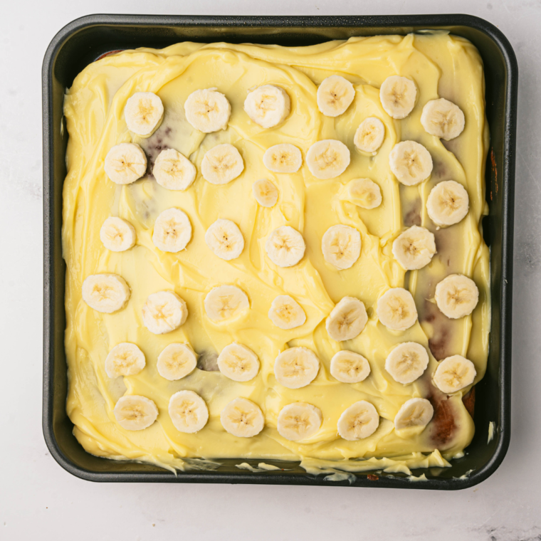 "Topping the Air Fryer Banana Poke Cake with whipped cream and banana slices"