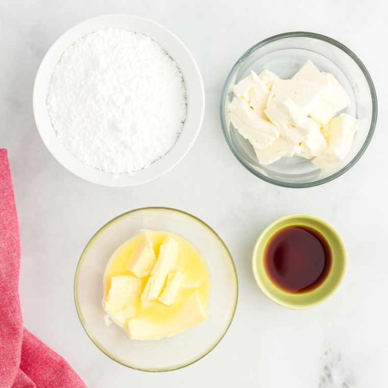 Cream cheese, butter, vanilla extract, and confectioners' sugar on a table