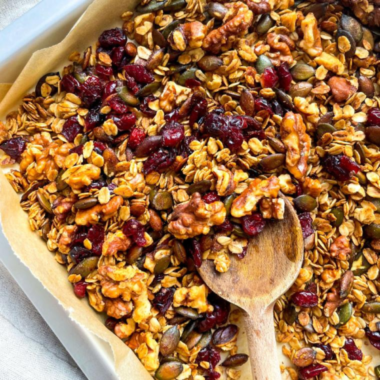 Cranberry Granola on a plate with a wooden spoon scooping some cooked air-fried cranberry granola up.