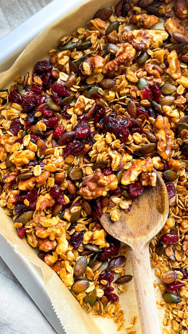 Cooked air fryer Cranberry Granola on a baking tray with a wooden spoon scooping some up