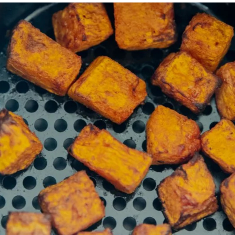 Close-up of air fryer frozen butternut squash cubes in the basket with browned caramelized edges