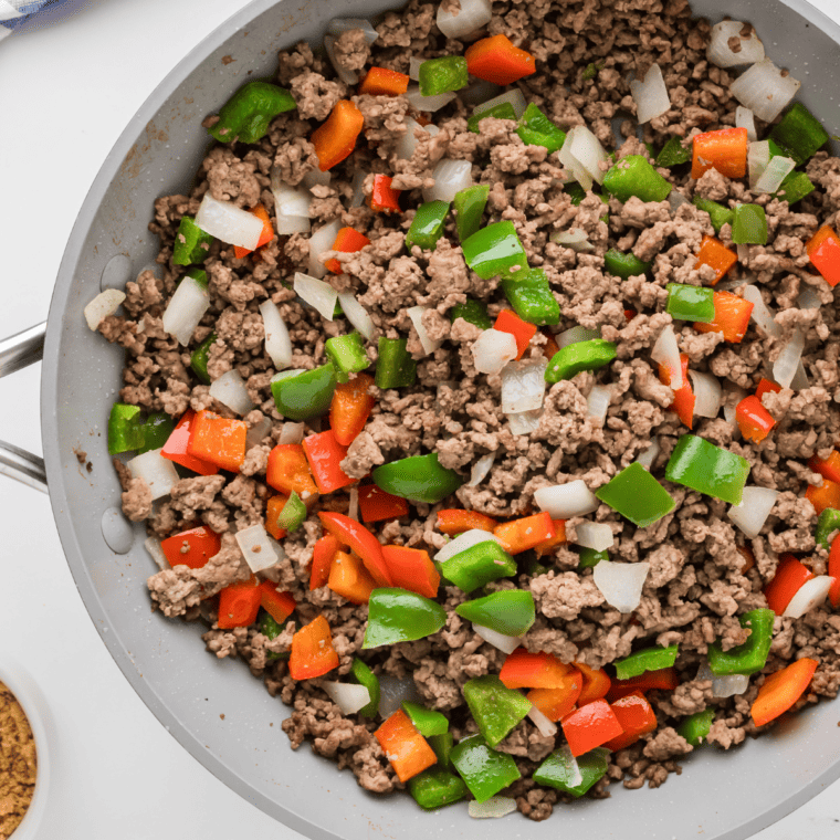 Diced onions, green and red bell peppers cooking in a skillet with seasonings and sauce.