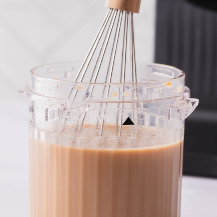 Milk being frothed in a small pitcher for a homemade peppermint mocha