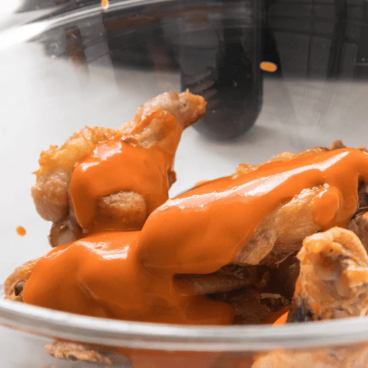 Crispy chicken wings being tossed with buffalo sauce in a large mixing bowl