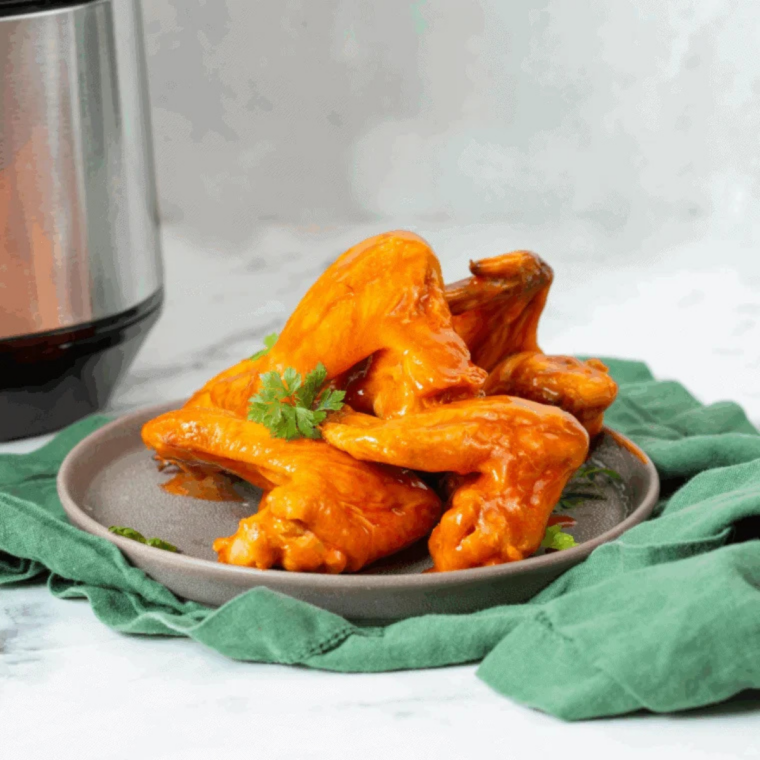 Ninja Crispi frozen chicken wings piled on a black plate with buffalo sauce and celery