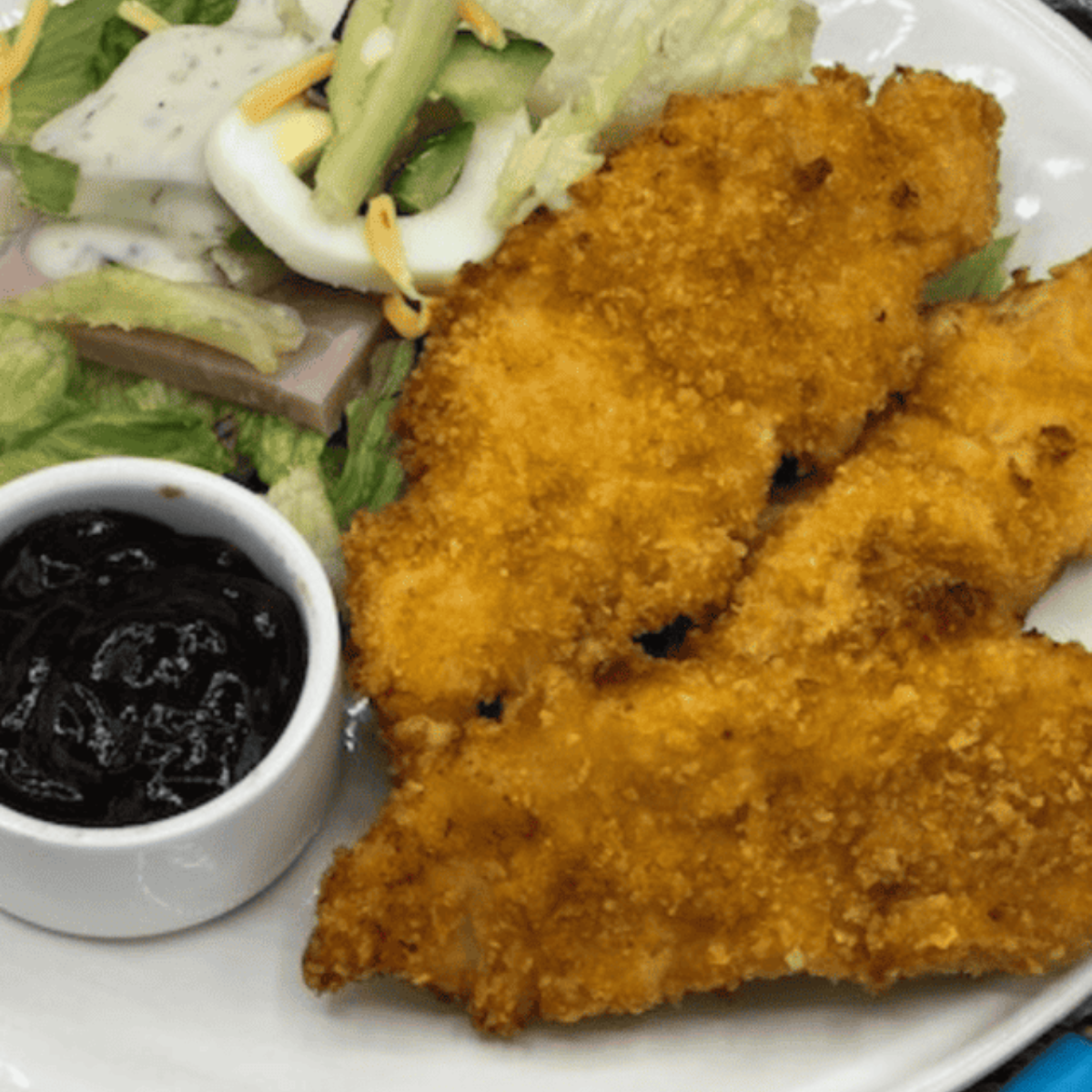 "Plate of southern-style Tyson chicken tenderloins served with a fresh salad, vegetables, and dipping sauce."