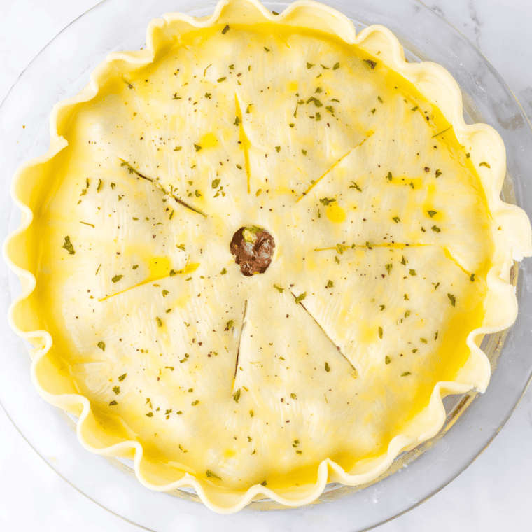 Pie crust round laid over beef filling in a white ramekin with edges crimped by hand
