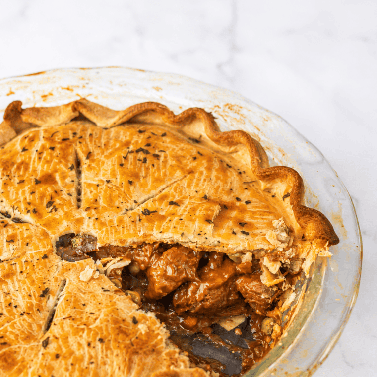 Air fryer beef pot pie in a white ramekin with a golden flaky crust cut open to show tender beef, carrots, and peas in brown gravy