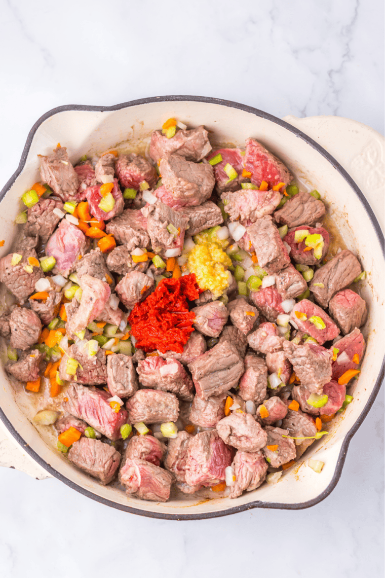Diced onion, celery, and carrot softening in a Dutch oven with browned beef fond on the bottom