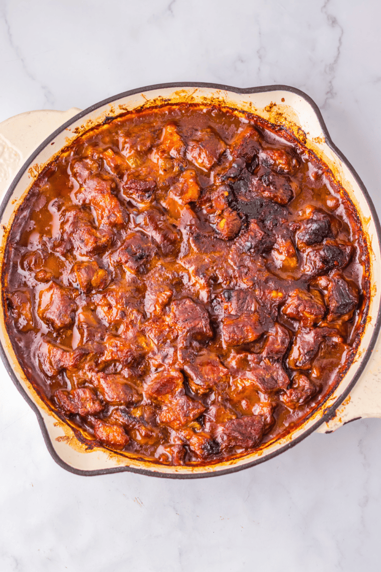 Beef and vegetables simmering in dark brown gravy in a covered Dutch oven