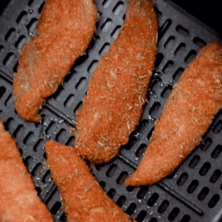 Air fryer basket with blackened chicken tenders arranged in a single layer.