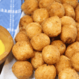 Overhead view of air fryer frozen hush puppies on a wooden serving board with dipping sauce