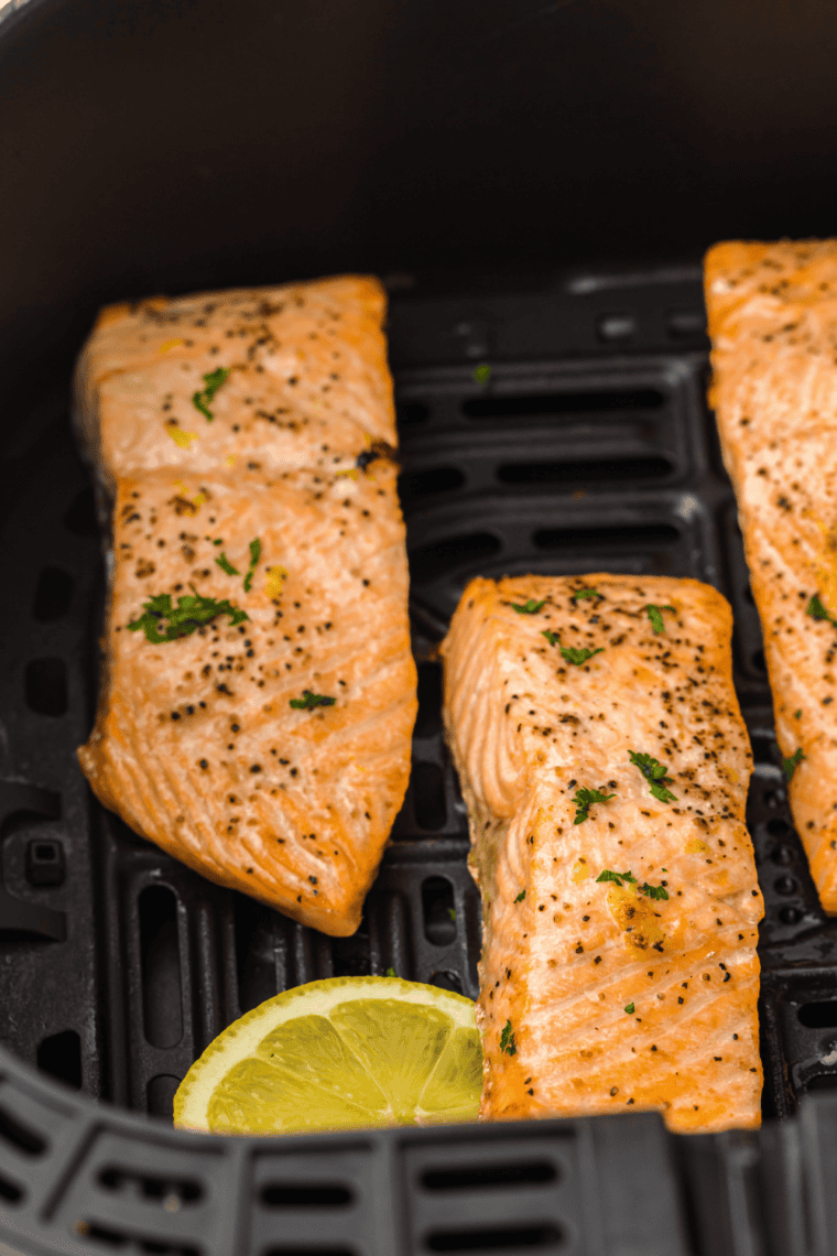 Golden-brown orange-glazed salmon fillet in an air fryer, garnished with fresh herbs.