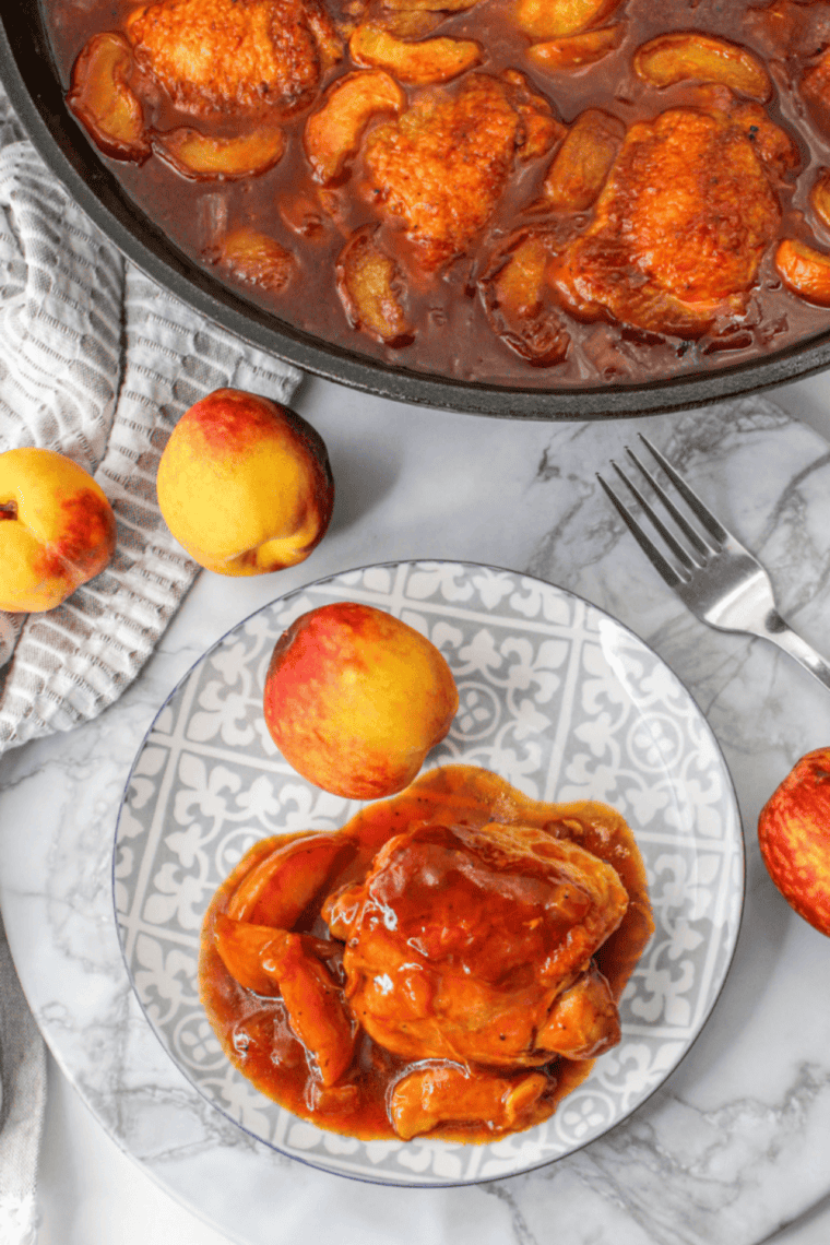 Jar of golden whiskey peach BBQ sauce with fresh peaches and spices on a wooden board.