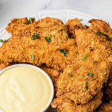 Plate of golden chicken nuggets with a small bowl of homemade Carolina Gold BBQ sauce for dipping