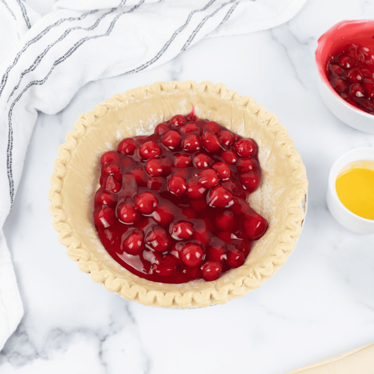 Thawing frozen pie crusts and placing one in the bottom of a pie dish, gently pressing it into place.