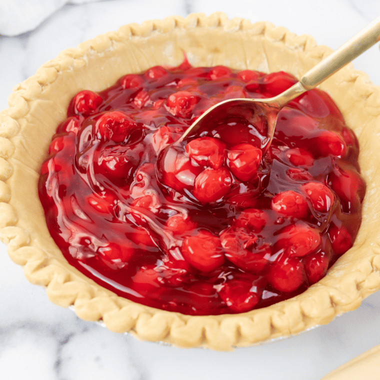 Scooping cherry pie filling into the prepared pie crust and spreading it evenly.