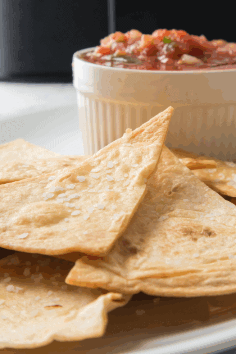 Crispy homemade Chili’s style tortilla chips served with salsa and guacamole on a wooden board.