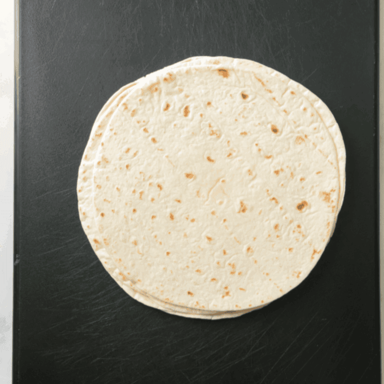 Stack of corn or flour tortillas on a cutting board.