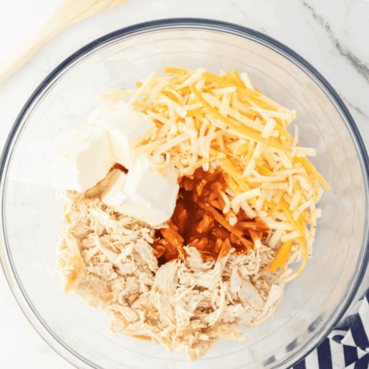 A mixing bowl filled with shredded chicken, cream cheese, cheddar, buffalo sauce, and green onions, fully combined into a creamy filling.