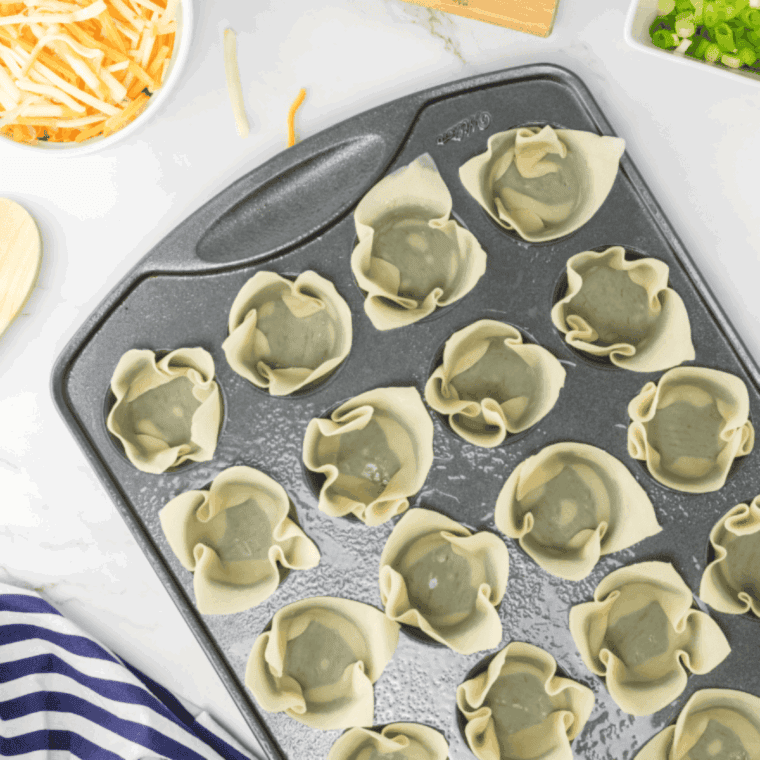 Wonton wrappers laid out on a countertop with a spoonful of buffalo chicken filling placed in the center of each.