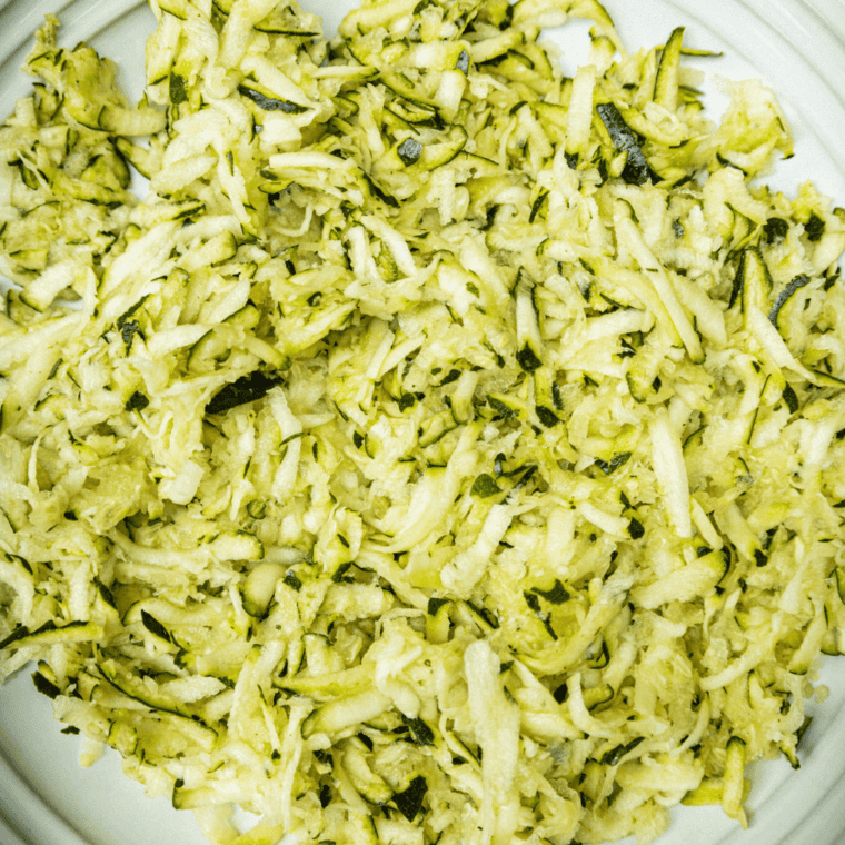 Grate fresh zucchini in a mixing bowl, preparing to make fritters.