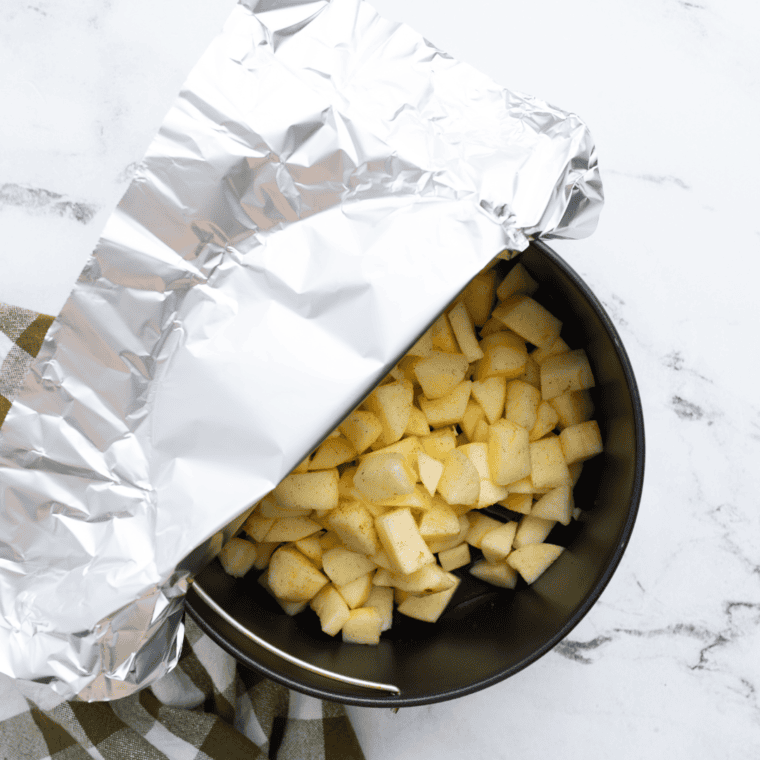 Seasoned chopped apples in a foil-covered bowl ready for air frying.