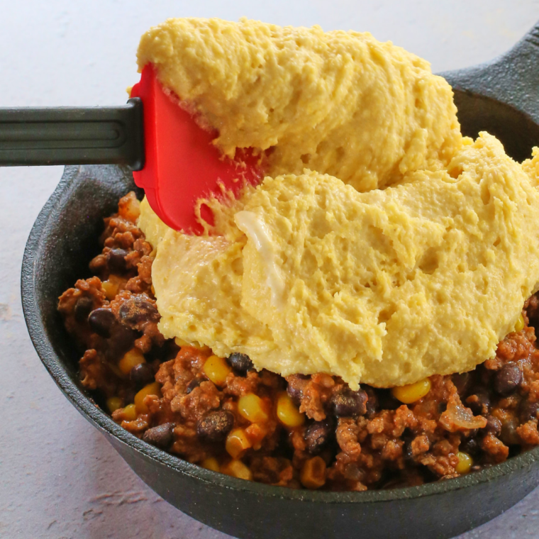 Cornbread batter spread over chili in a cast iron skillet before air frying