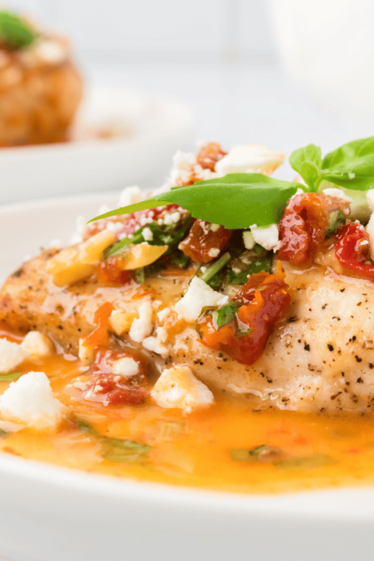 Copycat Carrabba’s Chicken Bryan with goat cheese, sun-dried tomatoes, and lemon basil sauce on a white plate.