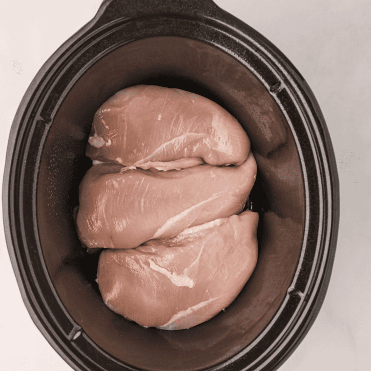 Raw chicken breasts in a slow cooker topped with Rotel, broth, and taco seasonings.