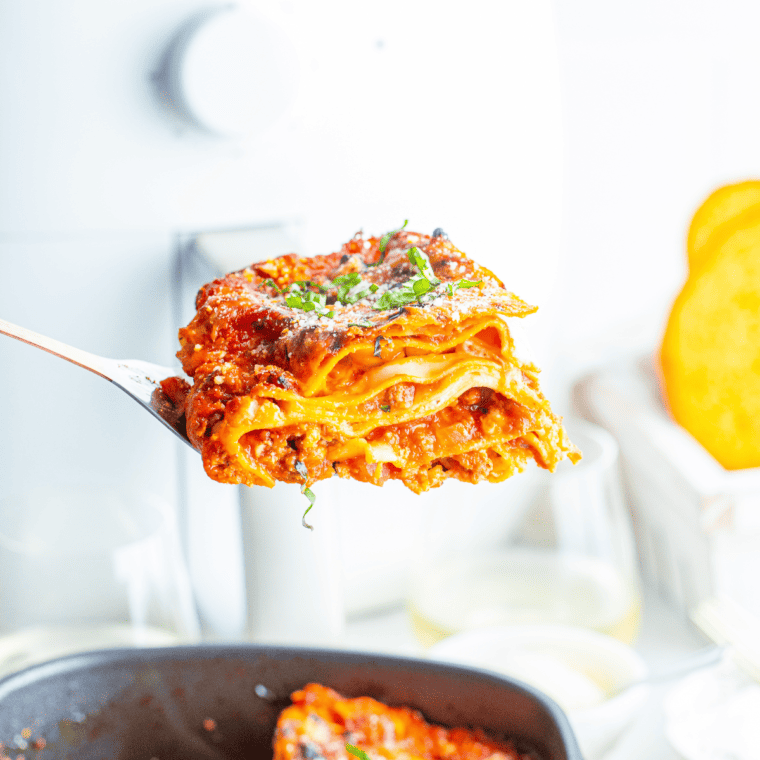 side view: a serving spoon lifting a slice of air fried lasagna out of air fryer
