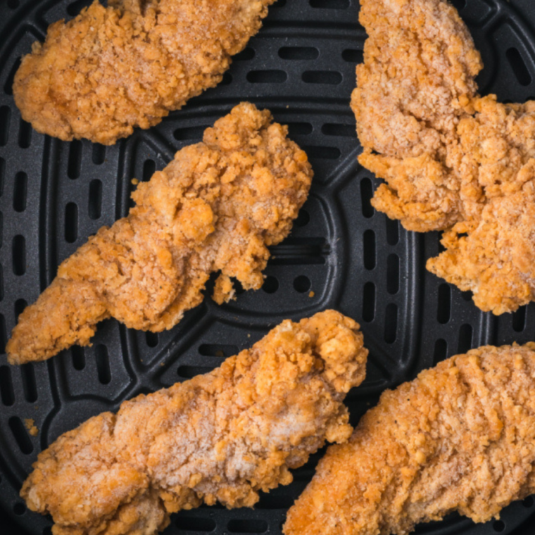 Chicken breast being placed in the air fryer basket for cooking.