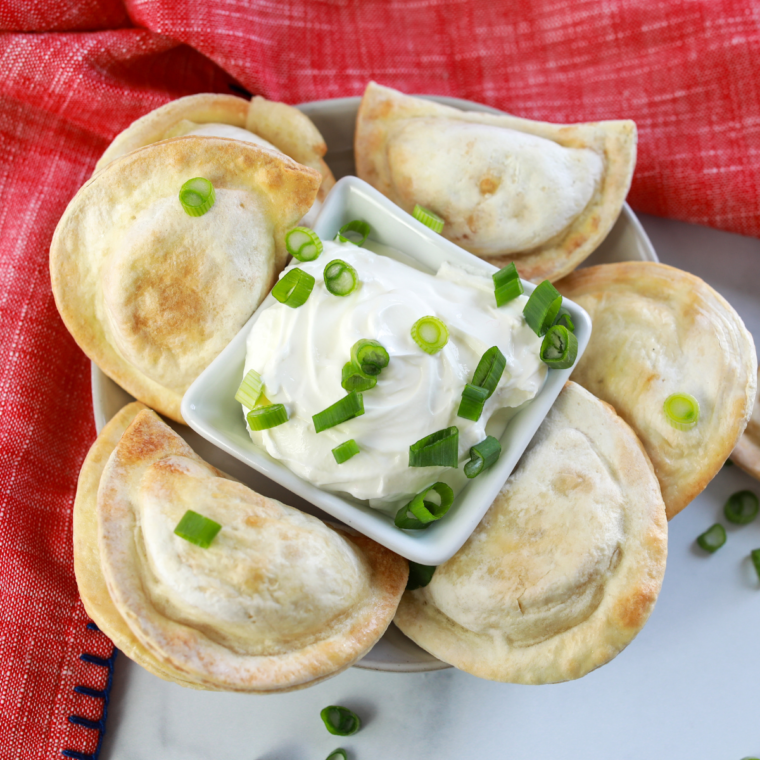 overhead: a plate of air fryer frozen pierogies with green onion on top and sour cream for dipping