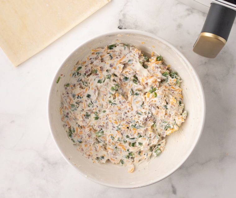 The filling in a large white bowl, showing cheese and diced jalapenos.