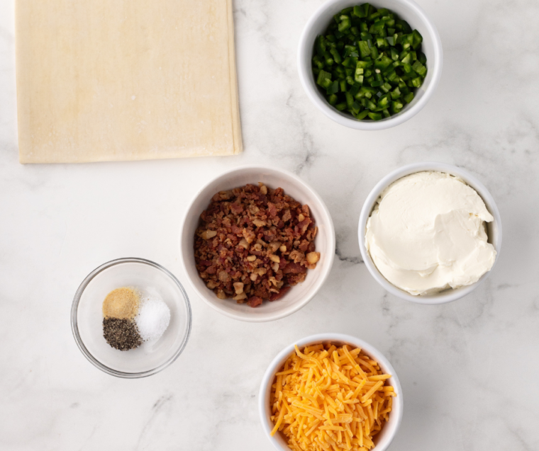 Ingredients for Jalapeno Popper Egg Rolls: A spread of ingredients needed for jalapeno popper egg rolls, including jalapenos, cream cheese, shredded cheese, egg roll wrappers, and spices.