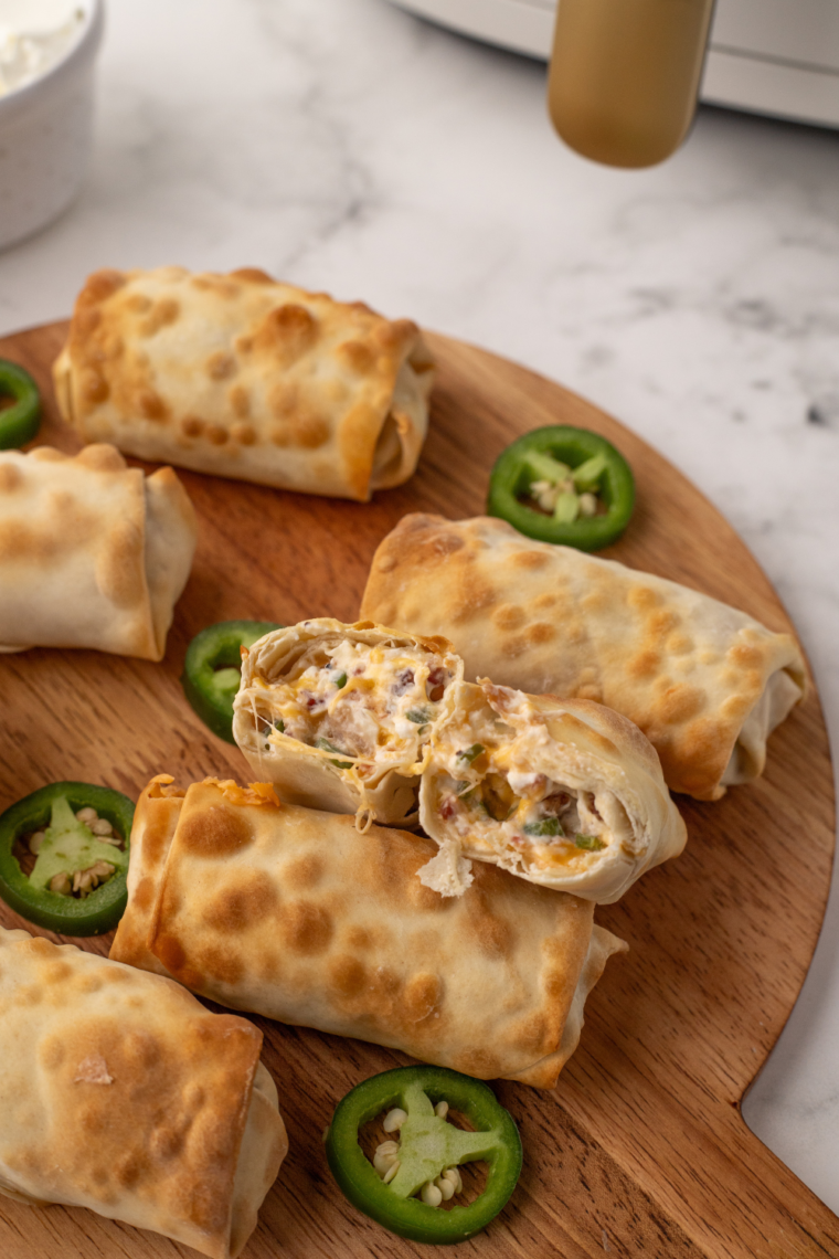 Air Fryer Jalapeno Popper Egg Rolls on a Wooden Cutting Board: A plate of golden brown, crispy air fryer jalapeno popper egg rolls neatly arranged on a rustic wooden cutting board, showcasing their crunchy texture and stuffed filling.