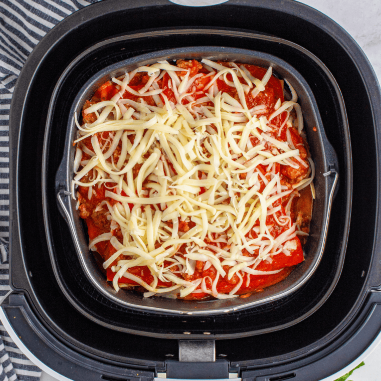 overhead process shot: adding shredded cheese to sauce layer of lasagna in air fryer