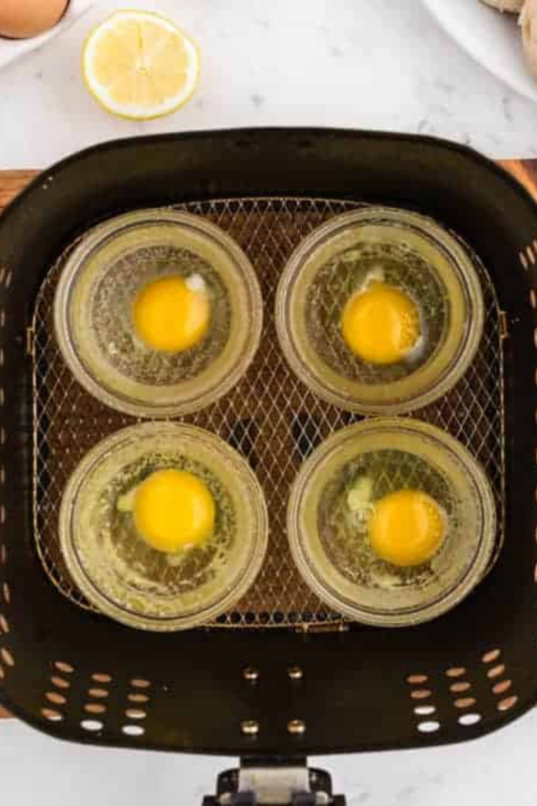 overhead closeup: four ramekins in an air fryer basket with raw eggs in each one