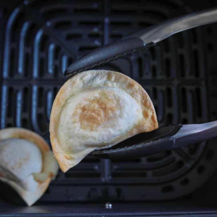 closeup: tongs holding an air fried frozen pierogie over the air fryer basket